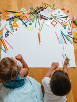 Kids drawing on floor on paper. Preschool boy and girl play on floor with educational toys - blocks, train, railroad, plane. Toys for preschool and kindergarten. Children at home or daycare. Top view